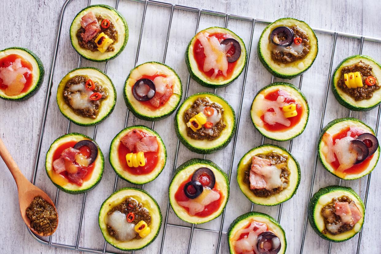 Grilled squash circles with tomato and pesto sauce, cheese, corn, olive and bacon on white table.