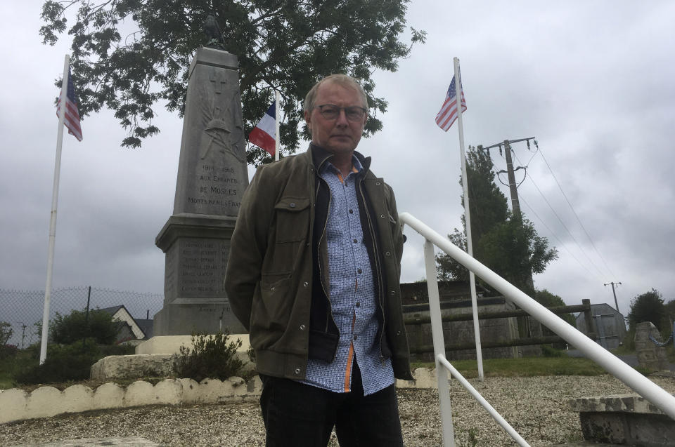 In this photo taken on Thursday, June 4, 2020, David Pottier, Mayor of the village of Mosles, Normandy, France, poses in front of a war monument after raising the American flags in remembrance of D-Day. In sharp contrast to the 75th anniversary of D-Day, this years 76th will be one of the loneliest remembrances ever, as the coronavirus pandemic is keeping nearly everyone from traveling. (AP Photo/Raf Casert)