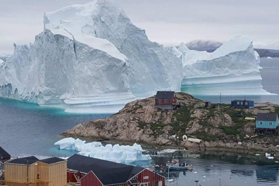 A giant iceberg is seen behind an Innaarsuit settlement, Greenland (REUTERS)