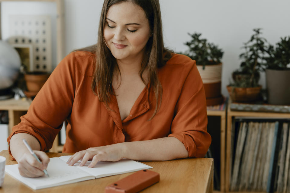 A smiling woman sitting at her desk and writing a journal.