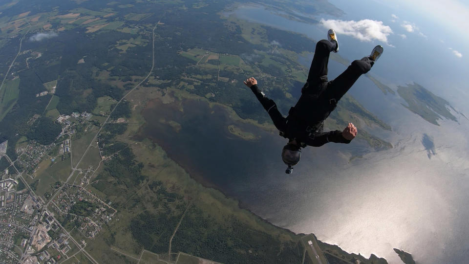 Aerial point of view of skydiver falling through clear skies toward a rural landscape