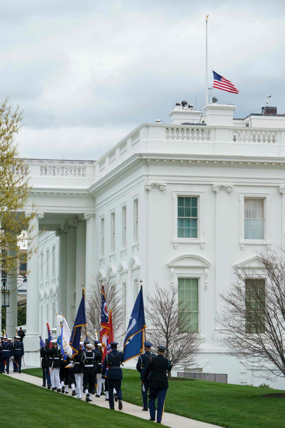 The flag above the White House flies at half staff in honor of the Indianapolis, Indiana shooting victims, in Washington, DC on April 16, 2021 as an honor guard setting up for the arrival for Japan's Prime Minister Yoshihide Suga is seen walking by.