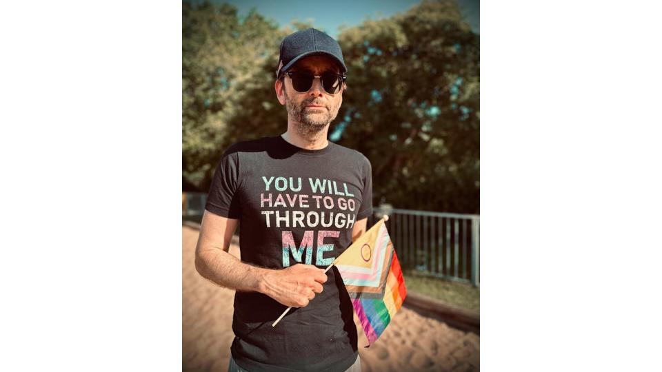 David Tennant wearing transgender rights T-shirt while holding Progress Pride flag 