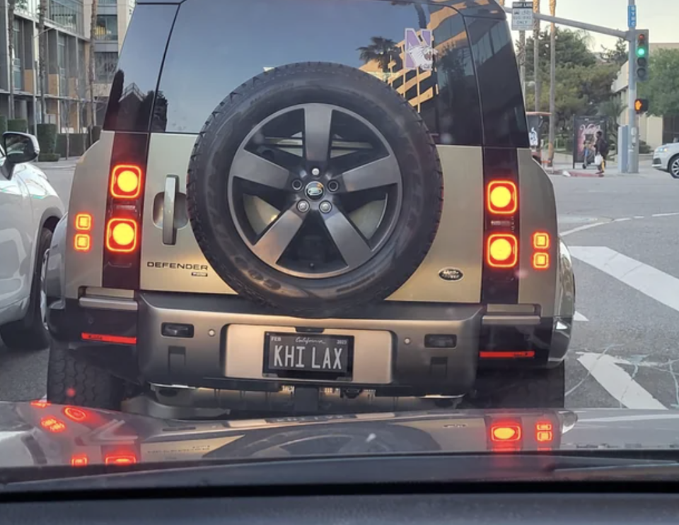Rear view of a Land Rover Defender at a traffic stop with personalized plate "KHI LAX"
