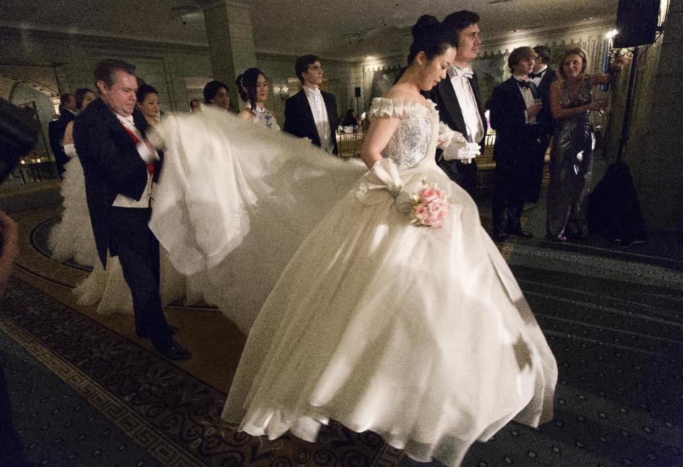 In this Thursday, Dec. 29, 2016 photo, a man adjusts a gown for Sabrina Xu, of Vancouver, Canada as she prepares to promenade at the International Debutante Ball in New York. (AP Photo/Mark Lennihan)