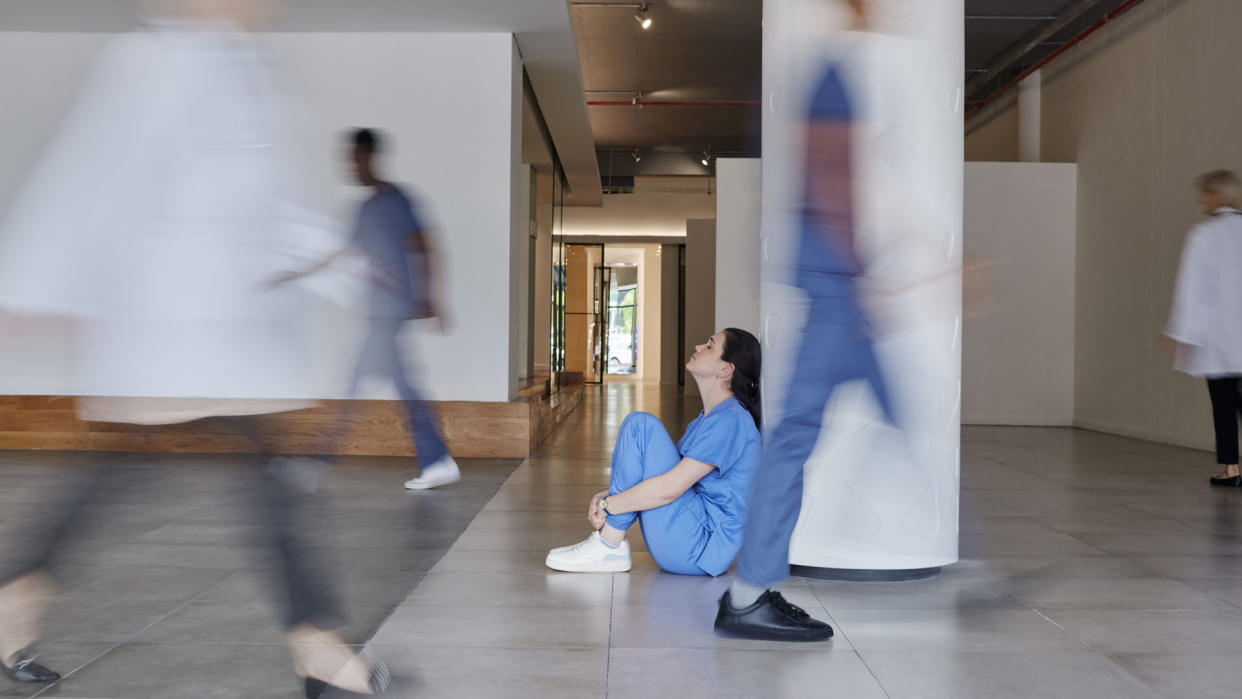  Shot of a young female doctor looking tired while working in a busy hospital  