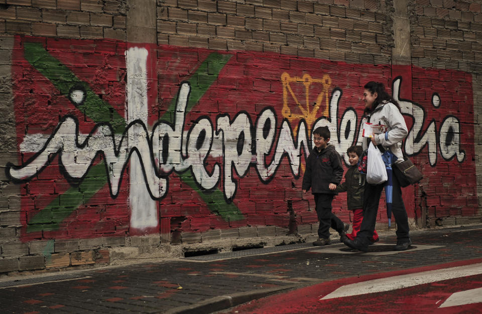 FILE - In this Jan. 12, 2011 file photo, people walk past a wall with painted words in Basque that reads: "Independence", in the small town of Alsasua, northern Spain. Josu Urrutikoetxea, the last known chief of ETA, the now-extinct Basque separatist militant group, goes on trial Monday Oct. 19, 2020 in Paris for terrorism charges that he deems “absurd” because of his role in ending a conflict that claimed hundreds of lives and terrorized Spain for half a century. (AP Photo/Alvaro Barrientos, File)