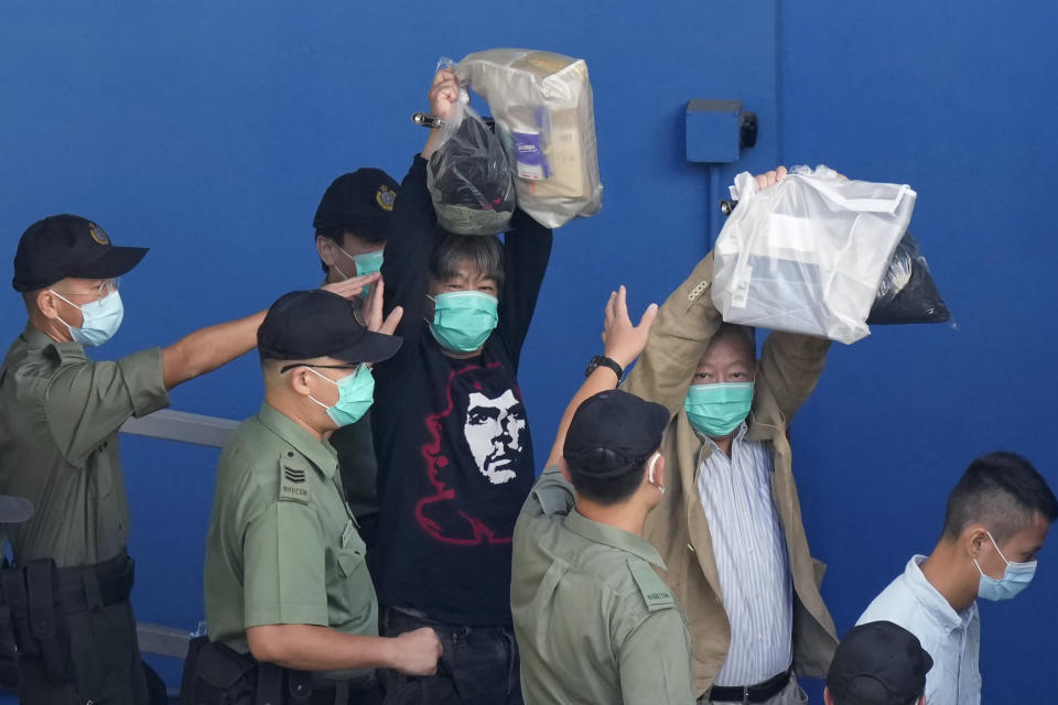 In this May 28, 2021, file photo, pro-democracy activists Leung Kwok-hung, known as "Long Hair," left, and Lee Cheuk-yan raise their hands as they are escorted by Correctional Services officers to a prison van for a court in Hong Kong. A national security law enacted in 2020 and COVID-19 restrictions have stifled major protests in Hong Kong including an annual march on July 1. (AP Photo/Kin Cheung, File)
