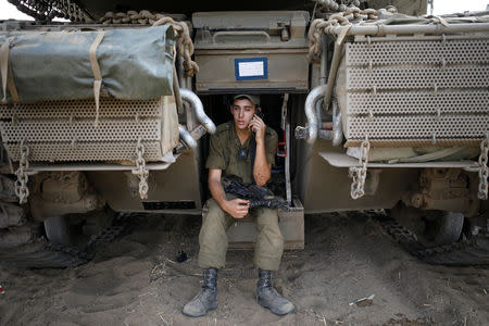 An Israeli soldier speaks on a phone as he sits on a tank positioned with other military armoured vehicles in an open area near Israel's border with the Gaza Strip October 18, 2018. REUTERS/Amir Cohen