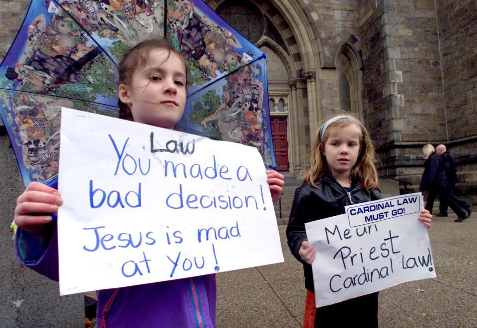 Six-year-old twins Allison (L) and Carolyn Monhagan of Hopkinton, Mass., protested Cardinal Bernard Law's handling of a pedophile priest scandal as the Catholic cardinal presided over a service at Boston's Cathedral of the Holy Cross in April 2002. Recent studies show that beginning in 2021, young women are leaving the church at equal or higher rates than young men, and experts say disillusionment over church sexual abuse scandals is among the likely factors.