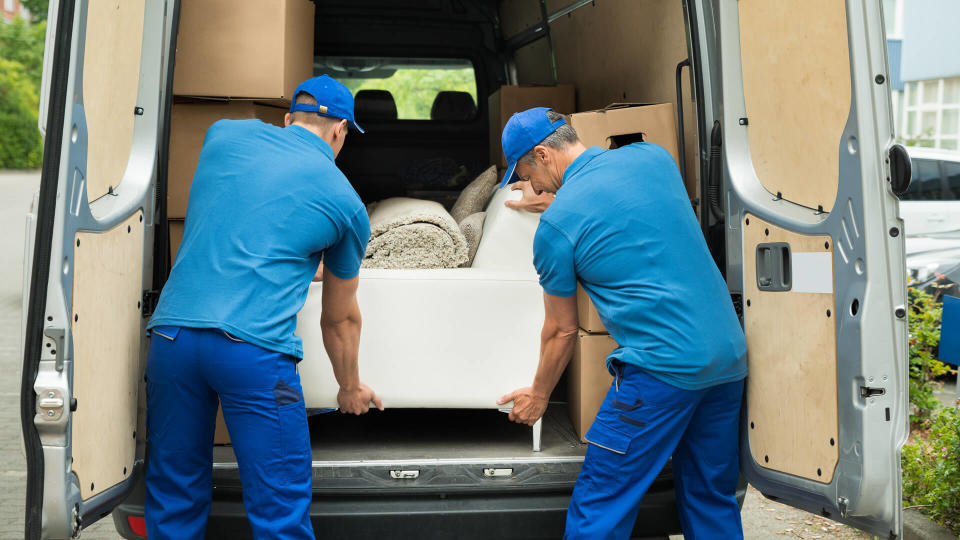 Two Male Workers In Blue Uniform Adjusting Sofa In Truck.