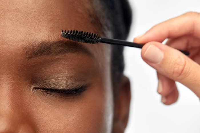 Close up of face of young woman and hand with mascara brush