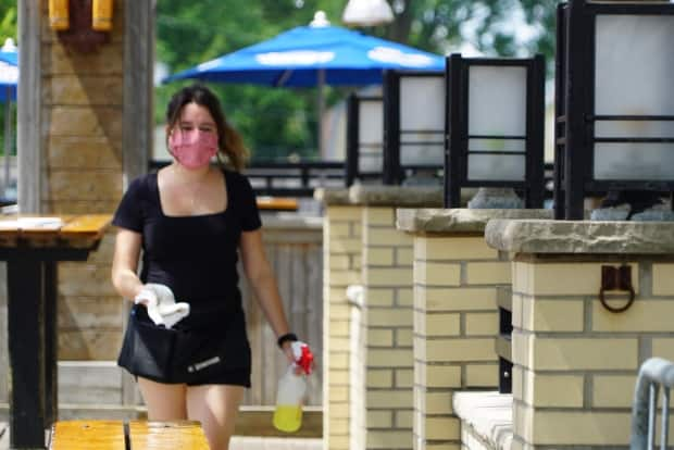 A masked waitress moves among the tables on an outdoor restaurant patio in London, Ont. Women with jobs in the food industry have been particularly hard hit during this pandemic. 