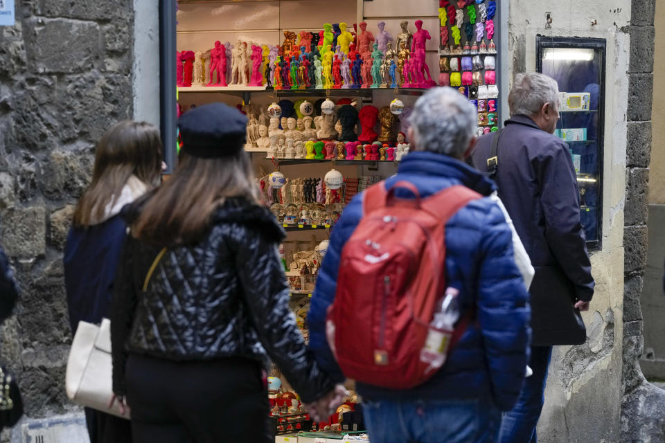 Personas pasan frente a una tienda de recuerdos con figuras de la estatua del David de Miguel Ángel del siglo XVI en un quiosco en el centro de Florencia, Italia, el lunes 18 de marzo de 2024. (Foto AP/Andrew Medichini)