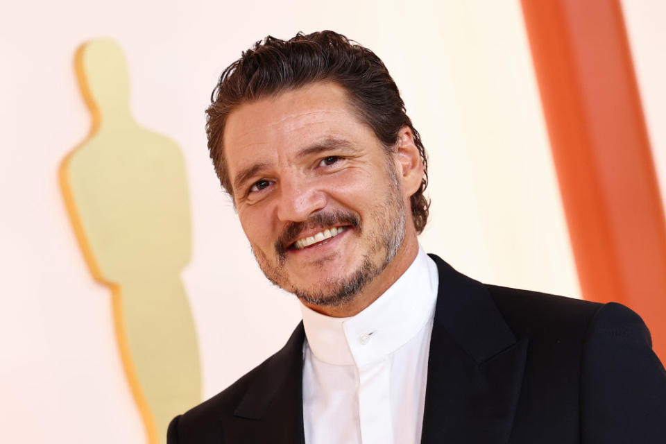 Pedro Pascal smiles on the red carpet in a black suit with a high-collared white shirt