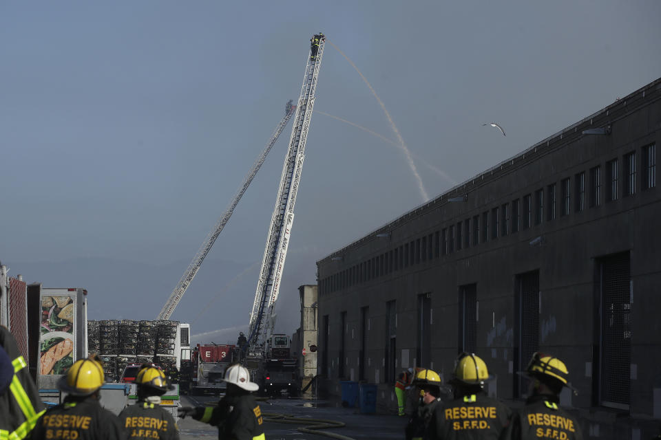A firefighter sprays into a warehouse after a fire broke out before dawn at Fisherman's Wharf in San Francisco, Saturday, May 23, 2020. Fire officials said no injuries have been reported Saturday morning and firefighters are making multiple searches to ensure no one was inside the building on Pier 45. (AP Photo/Jeff Chiu)