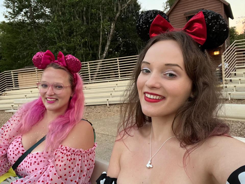 The author wearing a shoulderless dress and Minnie Mouse ears while taking a selfie with another woman who has pink hair and is also wearing Minnie Mouse ears.