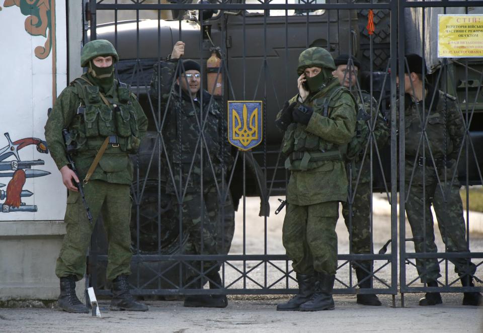 Military personnel, believed to be Russian servicemen, stand guard, with Ukrainian servicemen seen behind the gate, outside the territory of a Ukrainian military unit in the village of Perevalnoye outside Simferopol