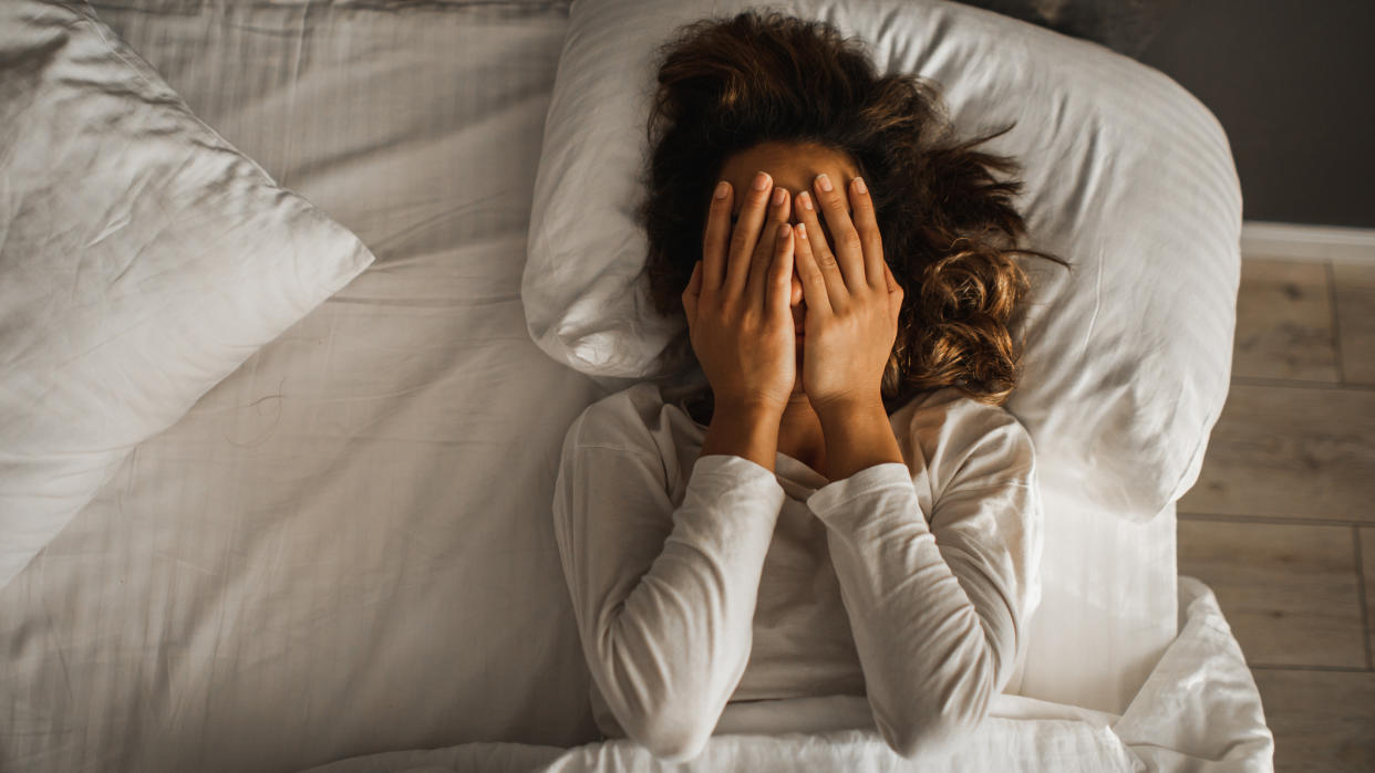  Woman lying in bed covering her face with her hands. 