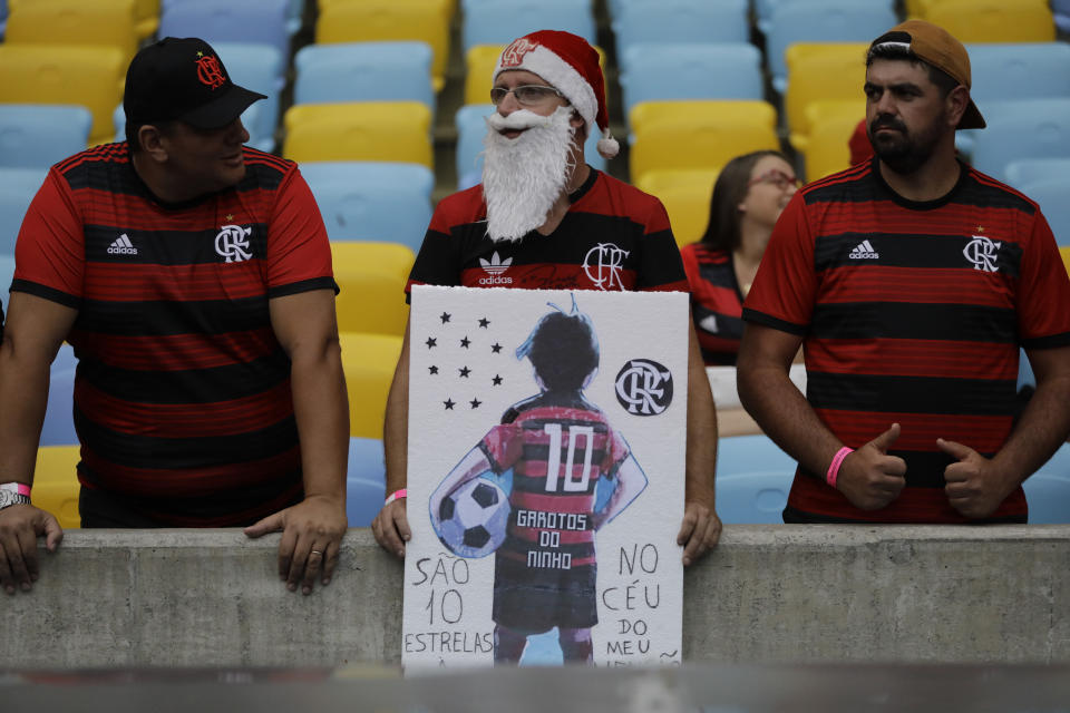 A man holds a drawing of a teenager in a Flamengo kit, as he waits for the start of a homage for the 10 teenage players killed by a fire at the Flamengo training center last Friday, at the Maracana Stadium, in Rio de Janeiro, Brazil, Thursday, Feb. 14, 2019, ahead of a soccer match between Flamengo and Fluminense. (AP Photo/Leo Correa)