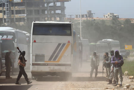 Rebel fighters stand guard as a convoy of buses (R) carrying Sunni rebels and civilians, who were evacuated from Zabadani and Madaya, as part of a reciprocal evacuation deal for four besieged towns, travel in al-Rashideen to journey towards rebel-held Idlib, Syria April 21 2017. REUTERS/Ammar Abdullah