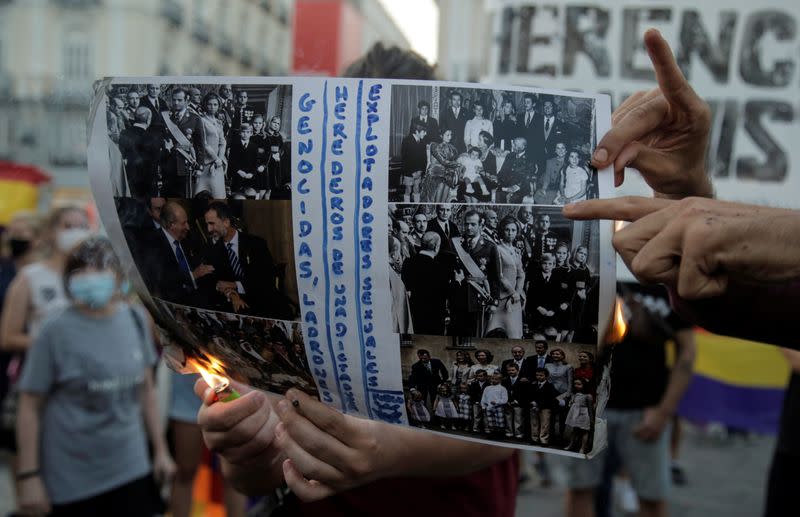 A protester destroys a picture of the royal family by a fire during a march against Spain's monarchy amid an investigation into Juan Carlos' involvement in a high-speed rail contract in Saudi Arabia, in Madrid