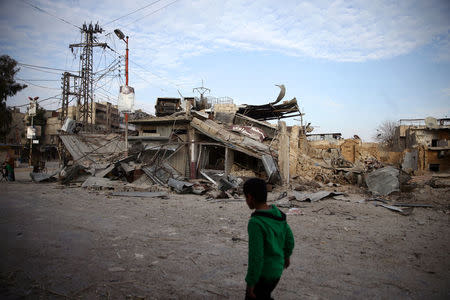 A child walks near damaged buildings in the besieged town of Douma, Eastern Ghouta, Damascus, Syria February 20, 2018. REUTERS/Bassam Khabieh