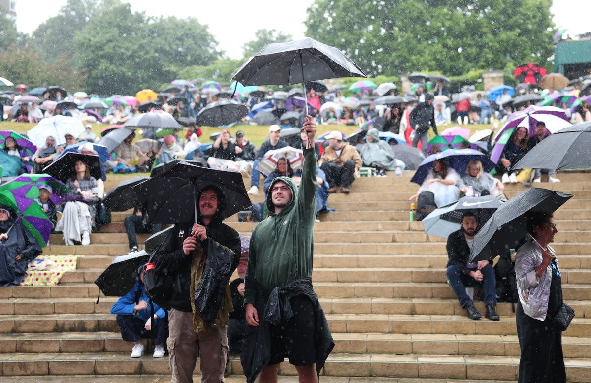 Spectators shelter from heavy rain as they sit on the steps to The Hill at Wimbledon (Getty Images)