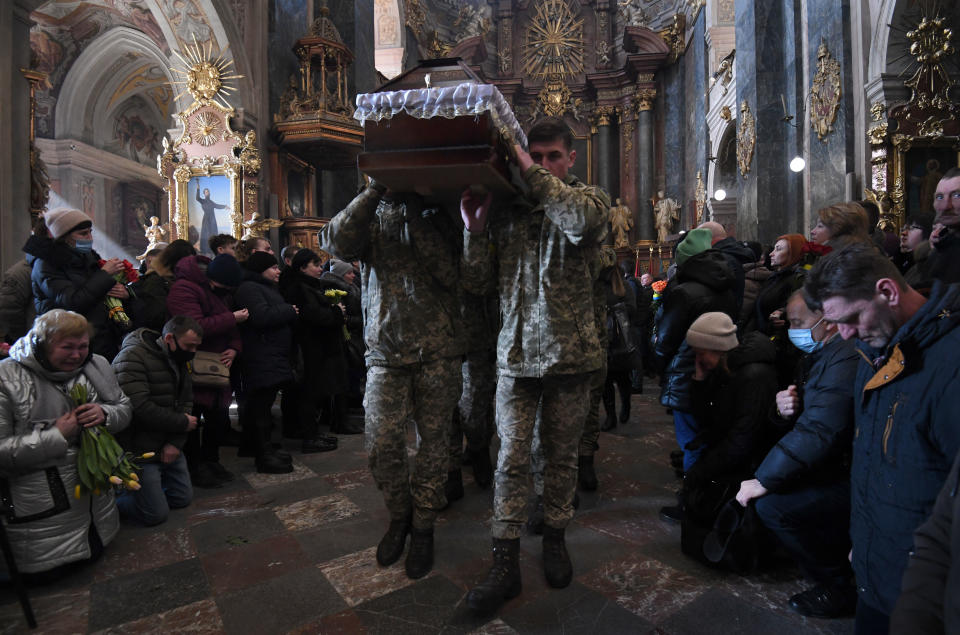 People kneel as soldiers carry the body of a killed comrade into a church.
