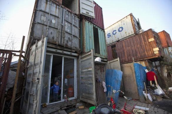 Un niño posa <b>en la puerta de su vivienda, un contenedor en Shanghái</b>. Estos contenedores, que albergan varias familias, fueron instalados por el propietario, que les cobra a las familias una renta mensual de 80 dólares. (REUTERS/Aly Song).