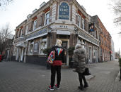 People stop to look at a sign depicting the image of Britain's Prince Harry and his wife Meghan, which hangs outside the Duke of Sussex pub near Waterloo station, London, Tuesday March 9, 2021. Prince Harry and Meghan's explosive TV interview has divided people around the world, rocking an institution that is struggling to modernize with claims of racism and callousness toward a woman struggling with suicidal thoughts. (AP Photo/Frank Augstein)