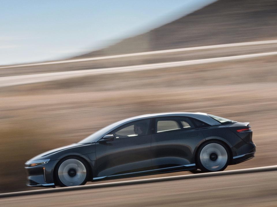 A Lucid Air Grand Touring driving against a blurry brown background.