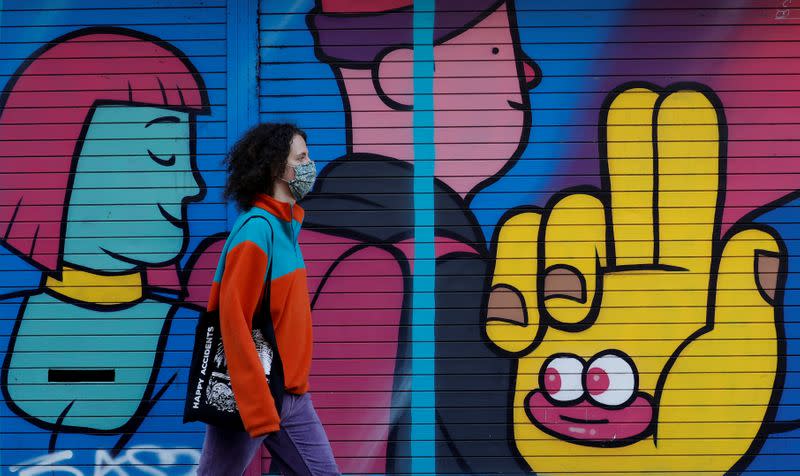 FILE PHOTO: A woman wears a face mask as she walks past a mural on a closed shop following the outbreak of the coronavirus disease (COVID-19) in Manchester, Britain