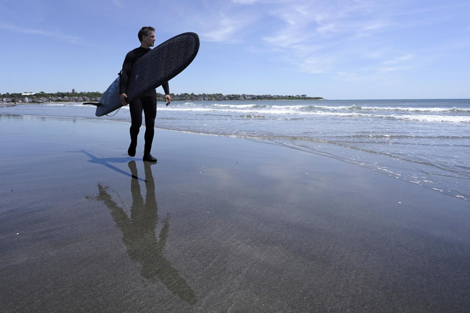 Dan Fischer, of Newport, R.I., carries his surfboard on Easton's Beach, in Newport, Wednesday, May 18, 2022. Fischer, 42, created the One Last Wave Project in January 2022 to use the healing power of the ocean to help families coping with a loss, as it helped him following the death of his father. Fischer places the names of lost loved ones onto his surfboards, then takes the surfboards out into the ocean as a way to memorialize the loved ones in a place that was meaningful to them. (AP Photo/Steven Senne)