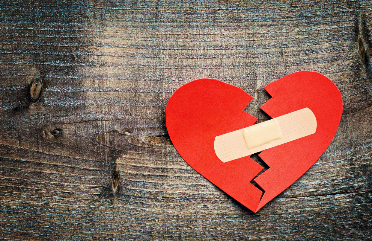 Red paper 'broken heart' with plaster on textured wood background.