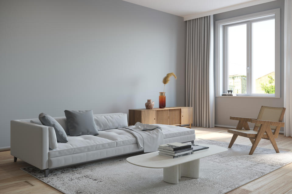 Modern living room with a sleek sofa, coffee table, wooden chair, and a sideboard under a large window with curtains, all on a minimalistic rug