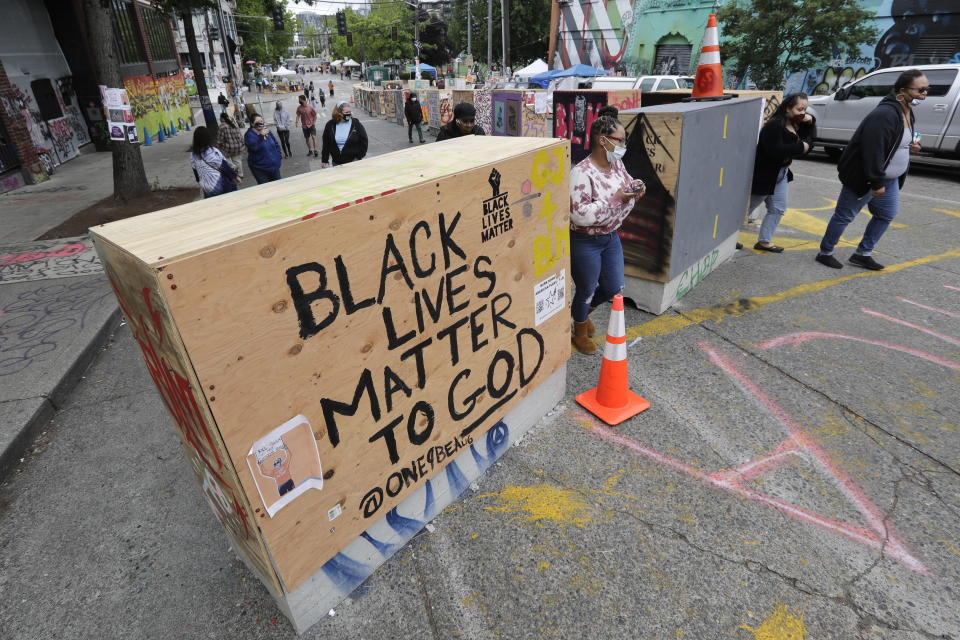 Pedestrians walk through barricades Sunday, June 21, 2020, in Seattle, where streets are blocked off in what has been named the Capitol Hill Occupied Protest zone. Police pulled back from several blocks of the city's Capitol Hill neighborhood near the Police Department's East Precinct building earlier in the month after clashes with people protesting the death of George Floyd. (AP Photo/Elaine Thompson)