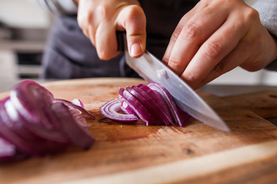 Cette photo repr&#xe9;sente une personne en train de couper des oignons rouges dans une cuisine.