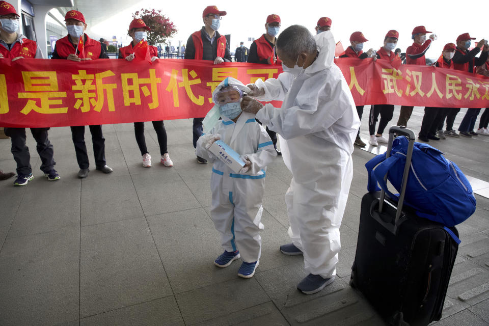 Travelers wearing face masks and suits to protect against the spread of new coronavirus walk past people holding a celebratory banner at Wuhan Tianhe International Airport in Wuhan in central China's Hubei Province, Wednesday, April 8, 2020. Within hours of China lifting an 11-week lockdown on the central city of Wuhan early Wednesday, tens of thousands people had left the city by train and plane alone, according to local media reports. (AP Photo/Ng Han Guan)