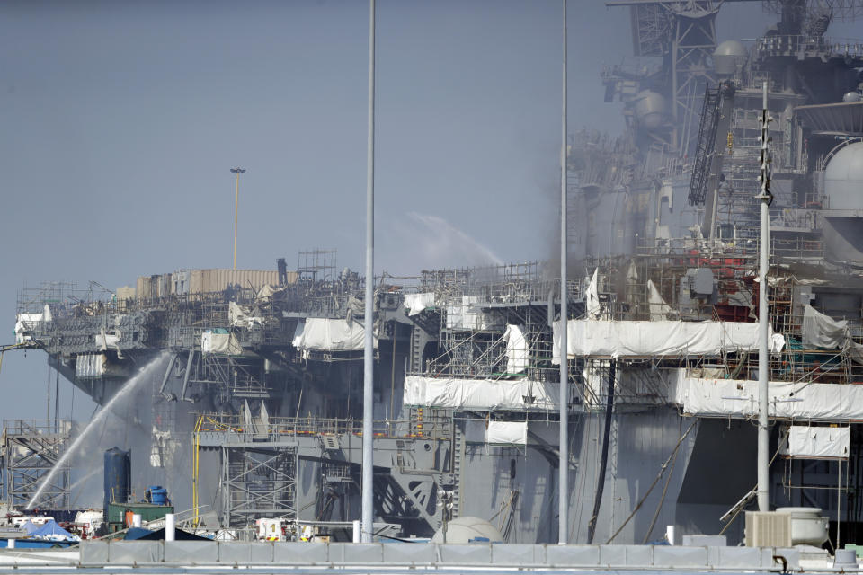 Fire crews spray water from the dock onto the side of the USS Bonhomme Richard, Tuesday, July 14, 2020, in San Diego. The battle to save the ship from a ravaging fire entered a third day in San Diego Bay on Tuesday with indications that the situation aboard the amphibious assault ship was improving. The U.S. Navy said in a statement late Monday that firefighters were making significant progress with the assistance of water drops by helicopters. (AP Photo/Gregory Bull)