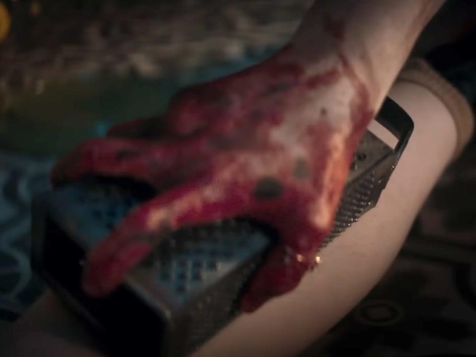A bloody hand holding a cheese grater against Beth's leg.