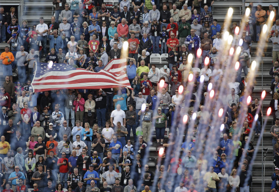 FILE - Fans cheer and wave a flag as fireworks explode during the playing of the national anthem before the start the Xfinity series auto race at Daytona International Speedway, Saturday, Feb. 21, 2015, in Daytona Beach, Fla. NASCAR has built itself around its traveling show, every weekend a super-charged event of concerts, camping and infield carousing that closes with a Cup race. The party has been canceled during the pandemic but the playoffs go on, starting Sunday, Sept. 6, 2020, without any of the pomp and circumstance. (AP Photo/John Raoux, File)