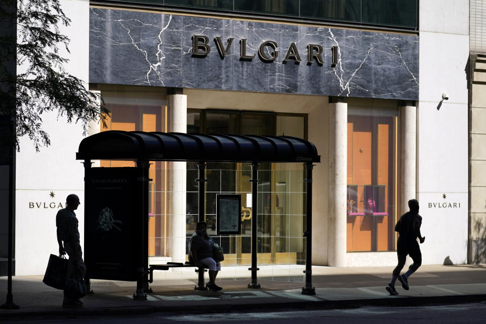 CORRECTS YEAR TO 2020 NOT 2019 Two pedestrians wait for a bus as another runs past the Italian luxury store Bulgari, known for its jewelry, watches, fragrances, accessories and leather goods, on Chicago's Magnificent Mile on Tuesday, Aug. 11, 2020. Store owners in and around Chicago's Michigan Avenue are asking themselves if of the economics and reputation of one America’s most prestigious shopping districts can rebound from the damage caused by looting this week. Businesses had been slowly reopening after pandemic-related shutdowns. (AP Photo/Charles Rex Arbogast)