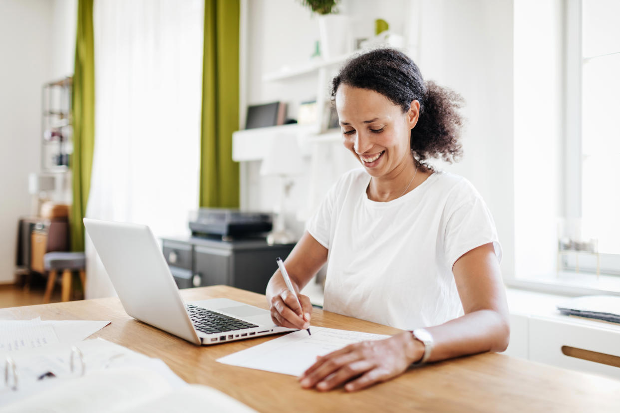 A single mom sitting in her kitchen at the table, taking some notes and working from home on her laptop.