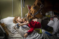 In this image released by World Press Photo, Thursday April 15, 2021, by Jeremy Lempin, Divergence-Images, titled Doctor Peyo and Mister Hassen, which won second prize in the Contemporary Issues category, shows Marion (24), who has metastatic cancer, embraces her son Ethan (7) in the presence of Peyo, a horse used in animal-assisted therapy, in the Selene Palliative Care Unit at the Centre Hospitalier de Calais, in Calais, France, on 30 November 2020. (Jeremy Lempin, Divergence-Images, World Press Photo via AP)