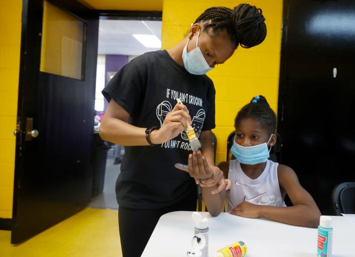 Amayah Martin, 21, of Detroit, paints gray on the hand of Jordyn McCall, 6, of Detroit, for an art class project at the What's Good In My Hood Outdoor Adventure Camp at the Tindal Recreation Center in Detroit on Thursday, June 30, 2022.