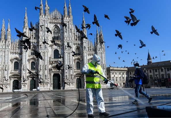 A man wearing protective gear, working for environmental services company AMSA, sprays disinfectant on Piazza Duomo in Milan.