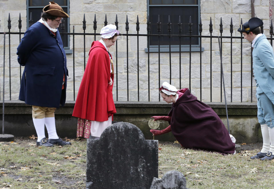 Actor-interpreters from the Boston Tea Party Ships and Museum, from left, Tim Lawton, Jillian Couillard, Sierra Grabowska and Stephen Chueka place commemorative markers, Tuesday, Nov. 27, 2018, at Central Burying Ground on Boston Common at the graves of participants in the Dec. 16, 1773 protest known as the Boston Tea Party. This year is the 245th anniversary of the protest during which colonists protesting taxation without representation threw British tea into Boston Harbor, considered a pivotal event that led to the American Revolution. (AP Photo/Elise Amendola)