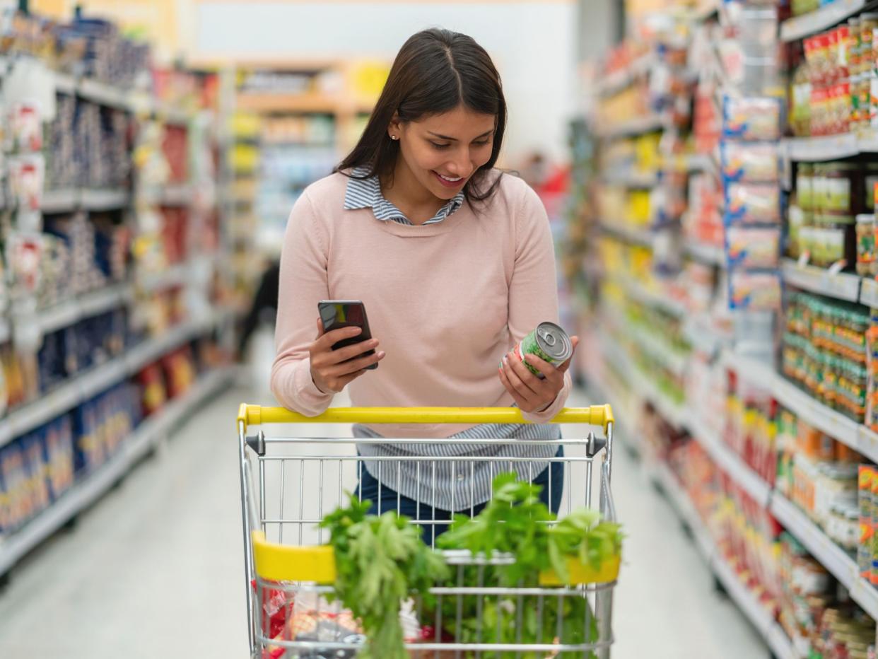 Low angle view of woman reading a review of product on smartphone at the supermarket while pushing cart