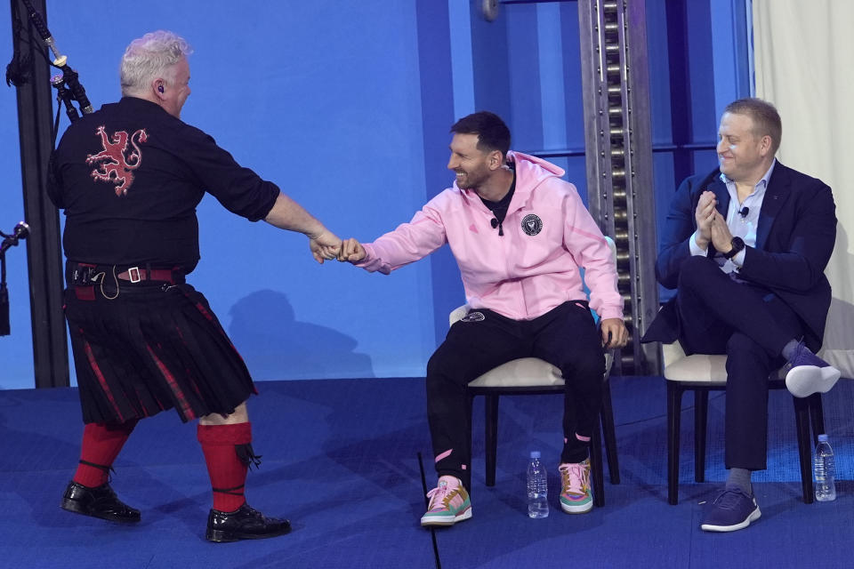 Inter Miami soccer player Lionel Messi, center, bumps fists with a member of the Red Hot Chilli Pipers bagpipe band, left, during a naming ceremony for Royal Caribbean International's new cruise ship, Icon of the Seas, Tuesday, Jan. 23, 2024, in Miami. Inter Miami CF has formed a partnership with the cruise line Royal Caribbean International. At right is Jason Liberty, president and CEO of the Royal Caribbean Group. (AP Photo/Lynne Sladky)